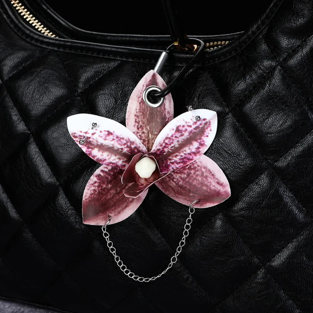 A realistic pink and purple phalaenopsis orchid flower keychain attached to a black quilted leather bag.
