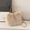 A light beige plush faux fur tote bag with a gold-toned crossbody strap resting on a white surface.