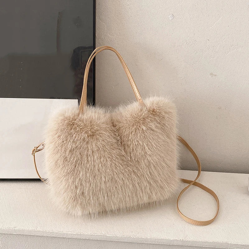 A light beige plush faux fur tote bag with a gold-toned crossbody strap resting on a white surface.
