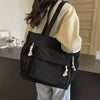 A black corduroy shoulder bag with zipper and tassels is shown carried on a person's shoulder.