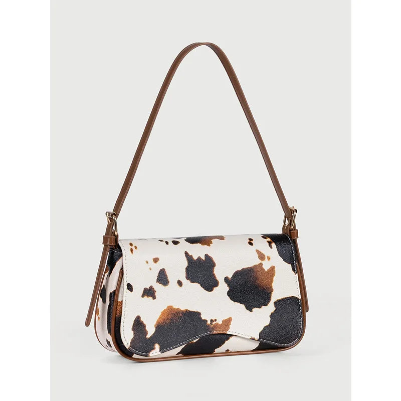 A brown leather single shoulder bag featuring a white and black cow print pattern.