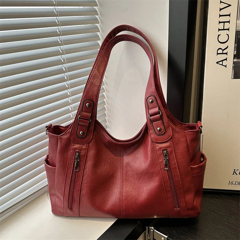 A maroon leather everyday large-capacity shoulder tote bag is displayed next to a window blind.