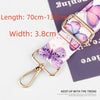A close-up of a pink and purple floral patterned nylon bag strap with a gold-toned buckle and lobster clasp.