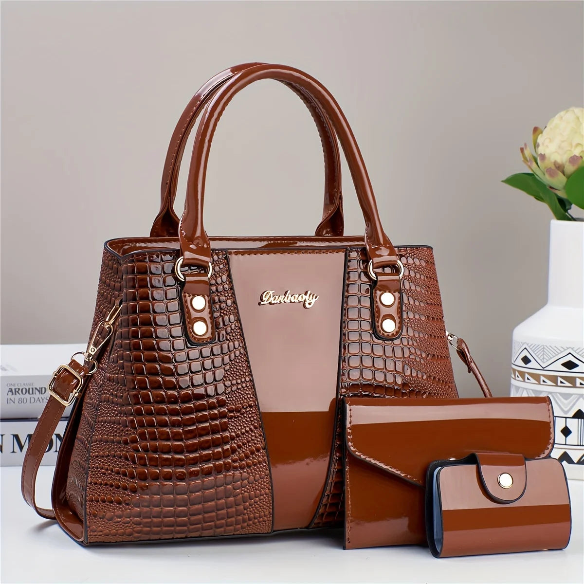 Bolso y cartera de cuero patentado con estampado de cocodrilo marrón sobre una superficie blanca.