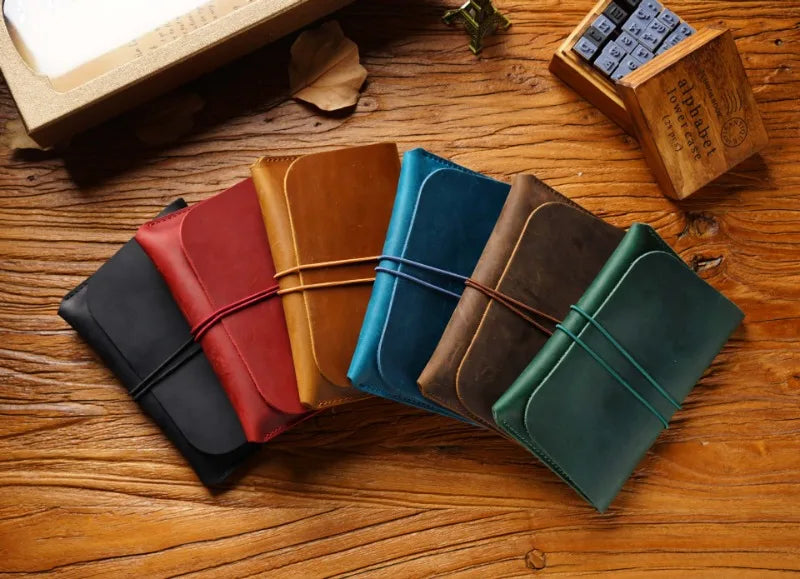 A collection of five minimalist full-grain leather passport holders and card wallets in various shades of brown, green, and r