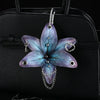 A realistic purple and blue orchid flower keychain attached to a black leather handbag.