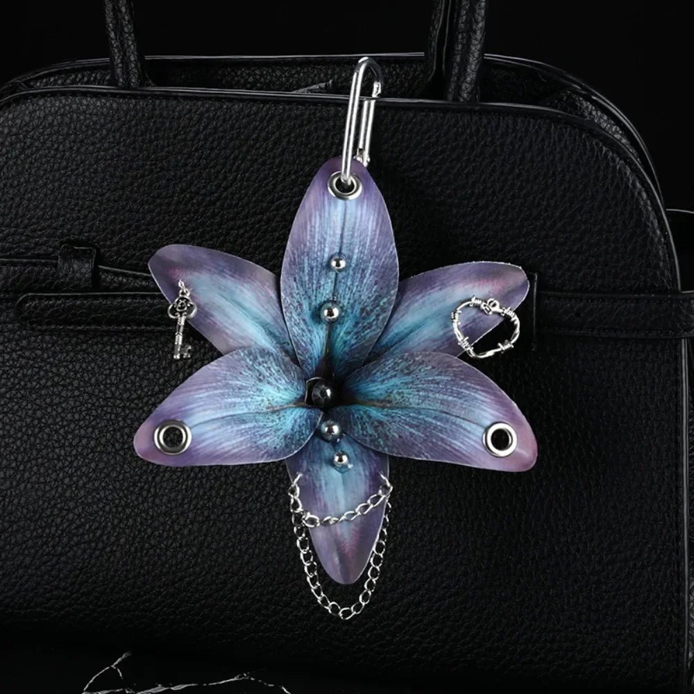 A realistic purple and blue orchid flower keychain attached to a black leather handbag.