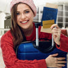 A smiling woman in a red sweater holds a blue suitcase and a passport holder.