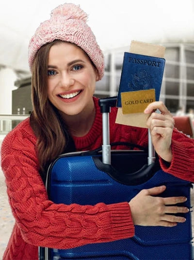 A smiling woman in a red sweater holds a blue suitcase and a passport holder.