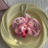 A realistic pink and white orchid flower keychain is displayed on a light yellow plate.