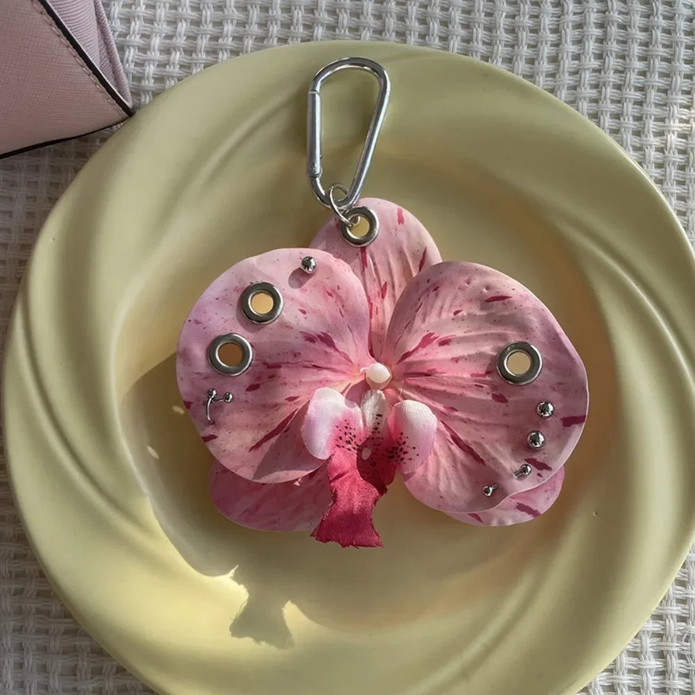 A realistic pink and white orchid flower keychain is displayed on a light yellow plate.