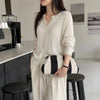A woman wearing a cream knit top and wide-leg pants holds a black and white striped clutch bag.