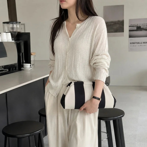 A woman wearing a cream knit top and wide-leg pants holds a black and white striped clutch bag.