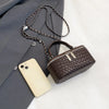 A dark brown woven crossbody bag with a silver chain strap resting next to a light-colored smartphone and a gray blazer.