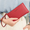 Eine Frau hält eine rote minimalistische PU-Leder-Geldbörse vor einem hellblauen Hemd und cremefarbenen Hosen.