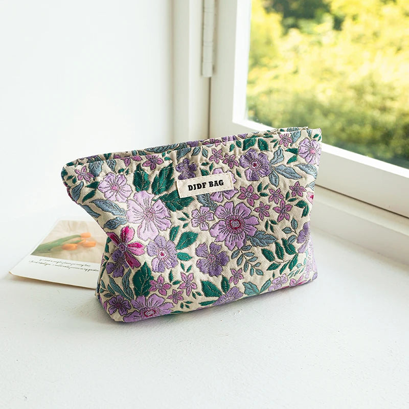 A purple floral canvas makeup bag with a small tag rests on a white windowsill next to a window.