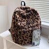 A brown and black leopard print plush backpack with multiple pockets resting on a white shelf.