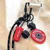 A red fitness keychain with a black D-shape nylon strap and a small black weight attached to a white leather bag.