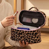 Una mano sostiene abierta una bolsa de maquillaje para viajar con estampado de leopardo rosa, mostrando el interior.
