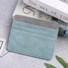 A light blue card holder wallet made of PU leather with a gray accent, resting on a gray surface next to a book.