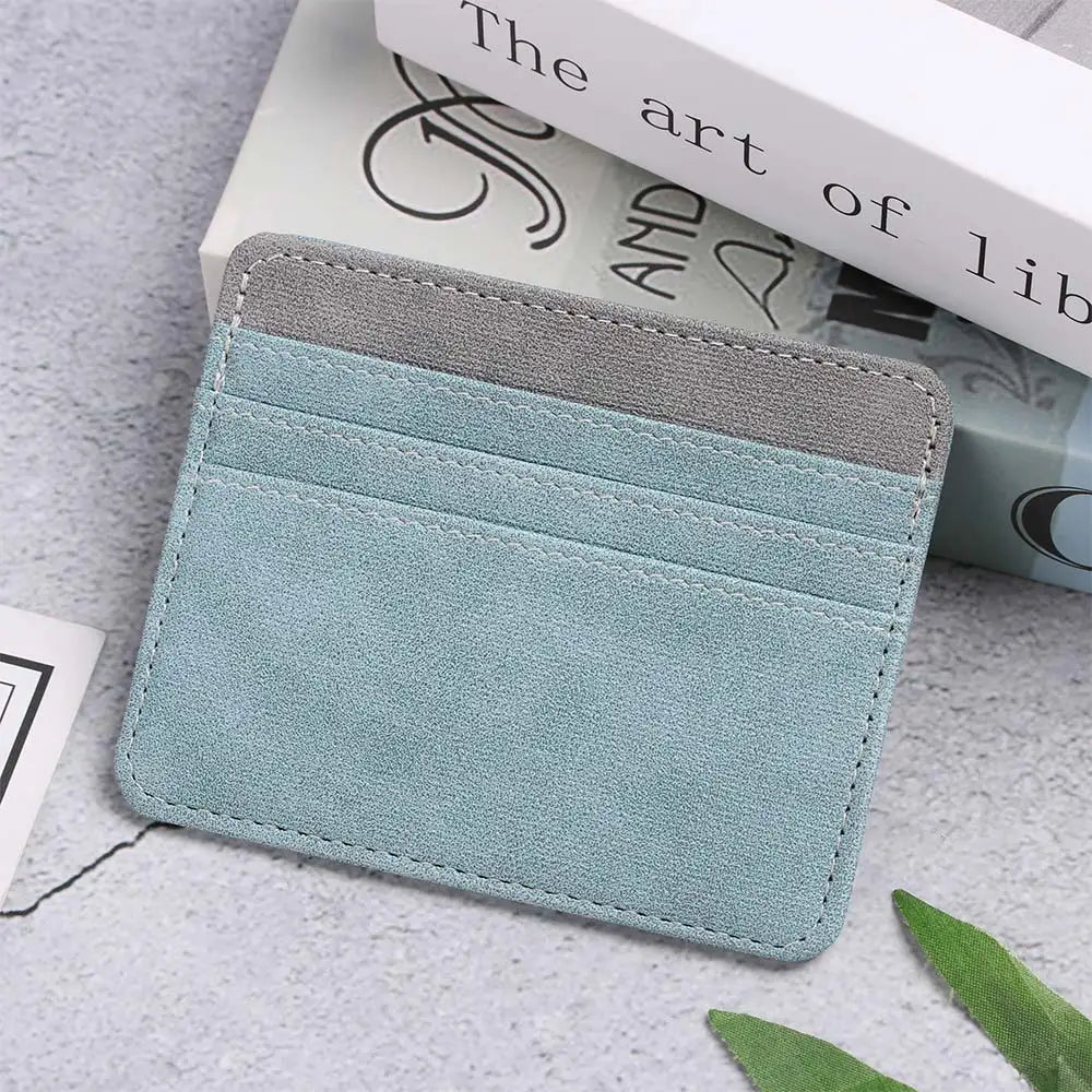 A light blue card holder wallet made of PU leather with a gray accent, resting on a gray surface next to a book.