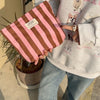 Una bolsa de lienzo con rayas rosadas y marrones sostenida por una persona que lleva una sudadera gris claro.