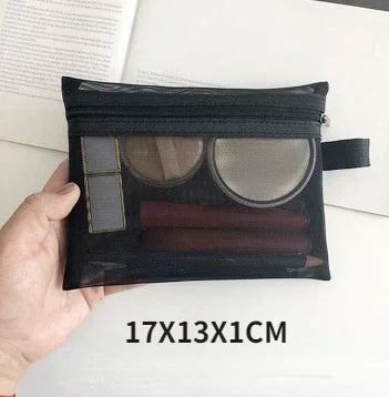 A black mesh cosmetic storage pouch with a clear window showing makeup products is held in a hand.