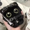 Colgante de gato negro de peluche con gafas y cadena de plata sostenido en una mano.
