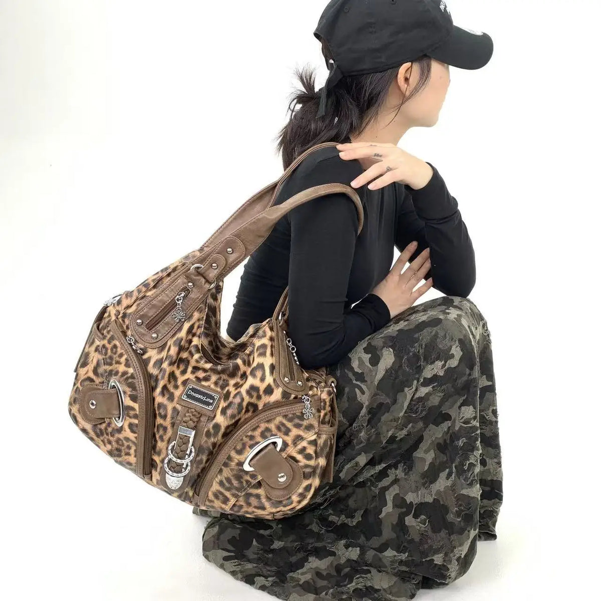 A woman wearing a black cap and black shirt holds a leopard print crossbody shoulder bag.
