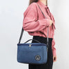 A woman holds a navy blue insulated portable lunch bag with a shoulder strap against a white background.