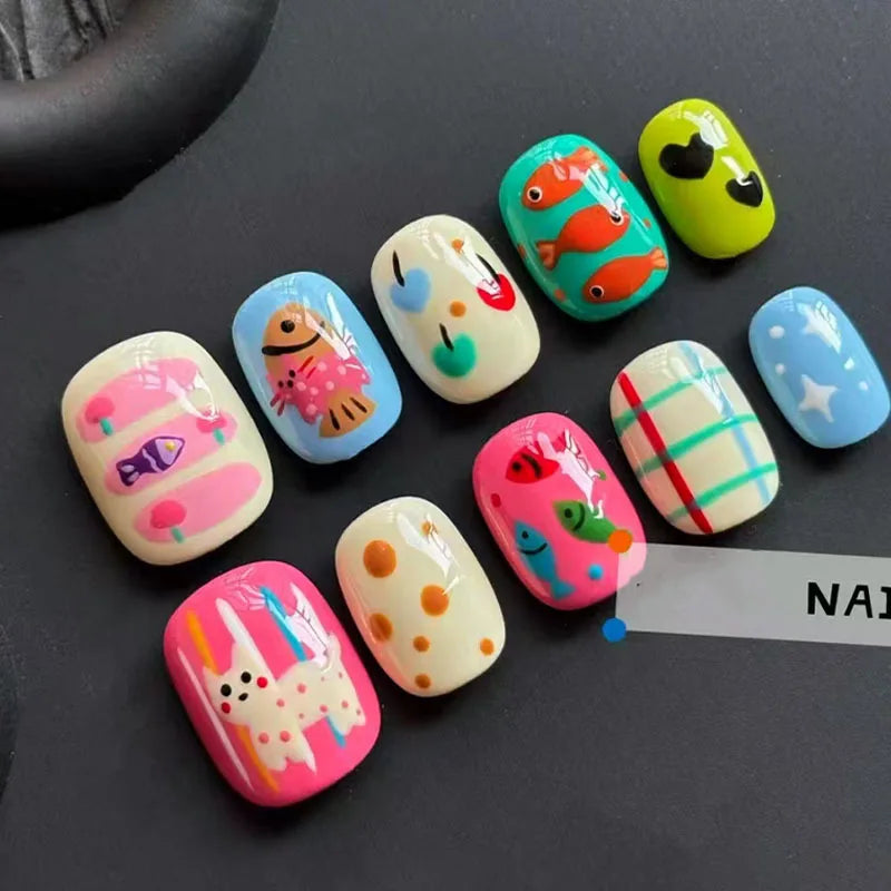A collection of colorful, cartoon-themed press-on nails in various bright and pastel shades arranged on a dark surface.