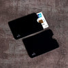 Two black anti-scan card sleeves are shown on a brown fabric, with a credit card visible next to them.