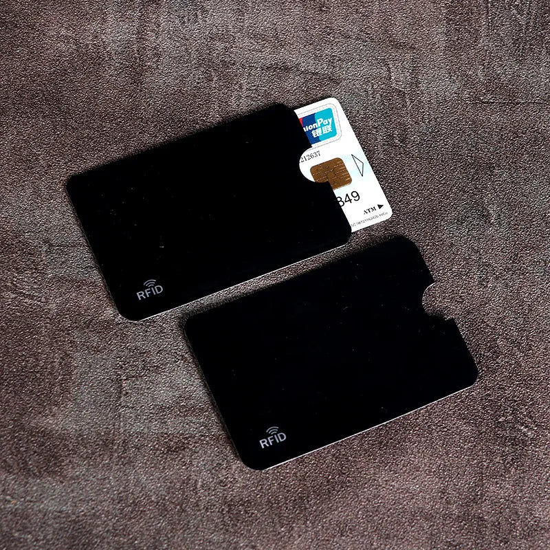 Two black anti-scan card sleeves are shown on a brown fabric, with a credit card visible next to them.