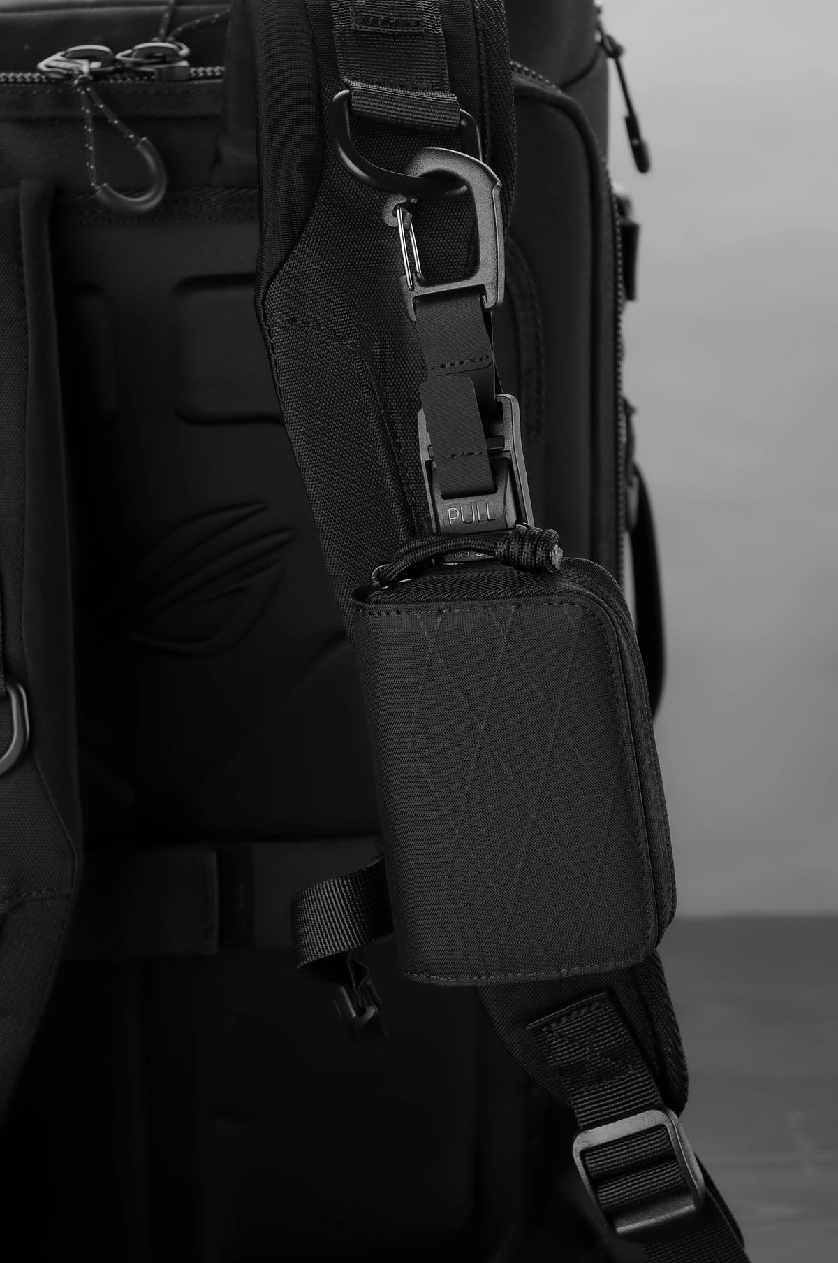 Close-up of a black RFID zipper wallet attached to a dark backpack strap.