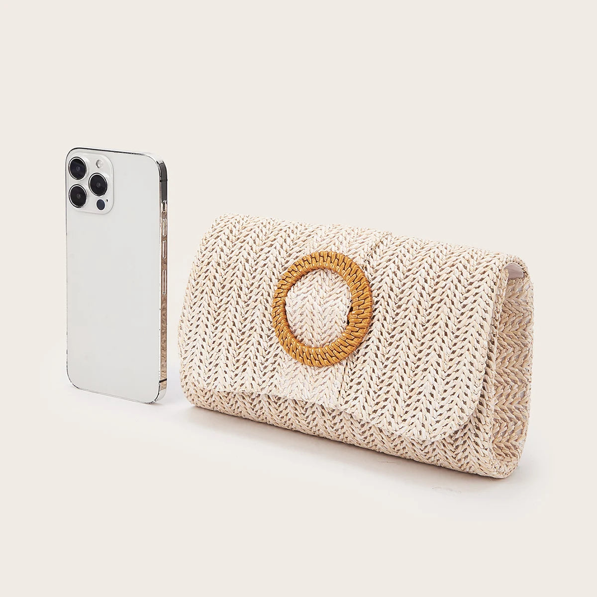 A woven straw envelope clutch with a round detail and detachable strap resting on a light background.