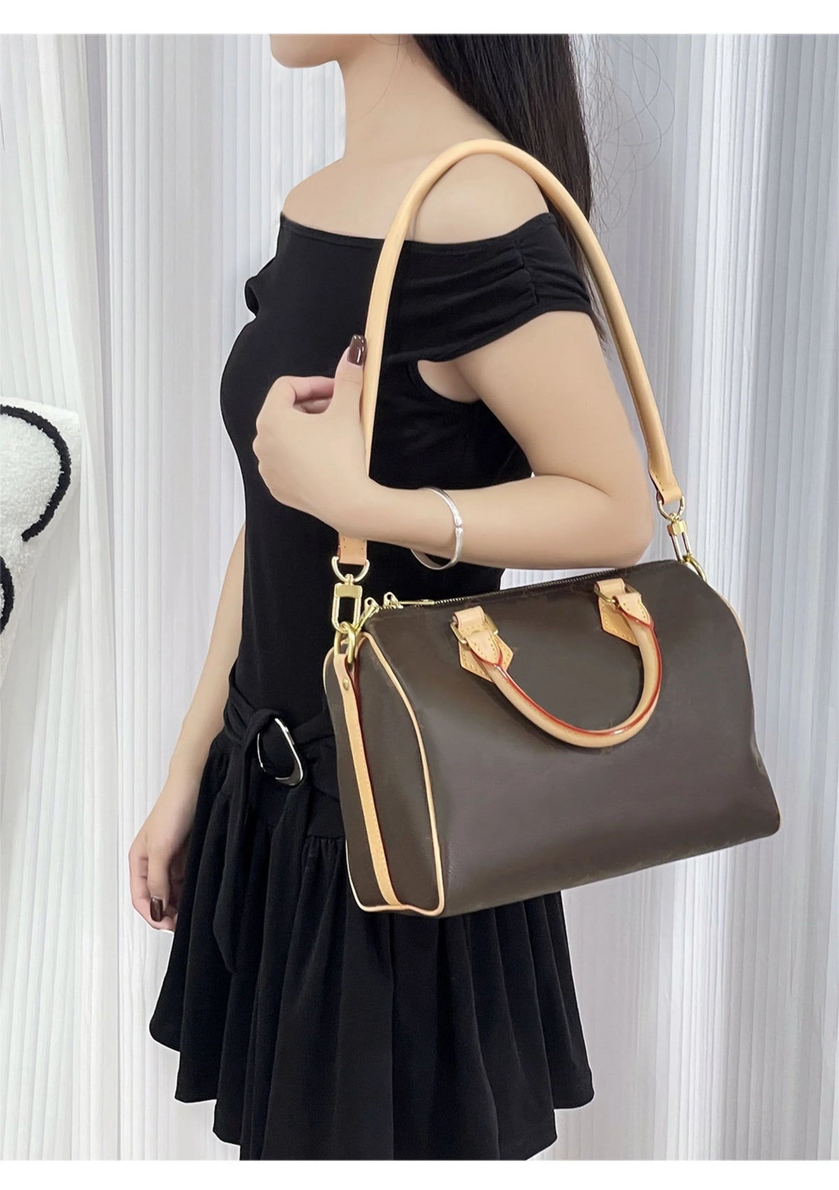 A woman models a brown leather shoulder bag with a tan strap against a white background.