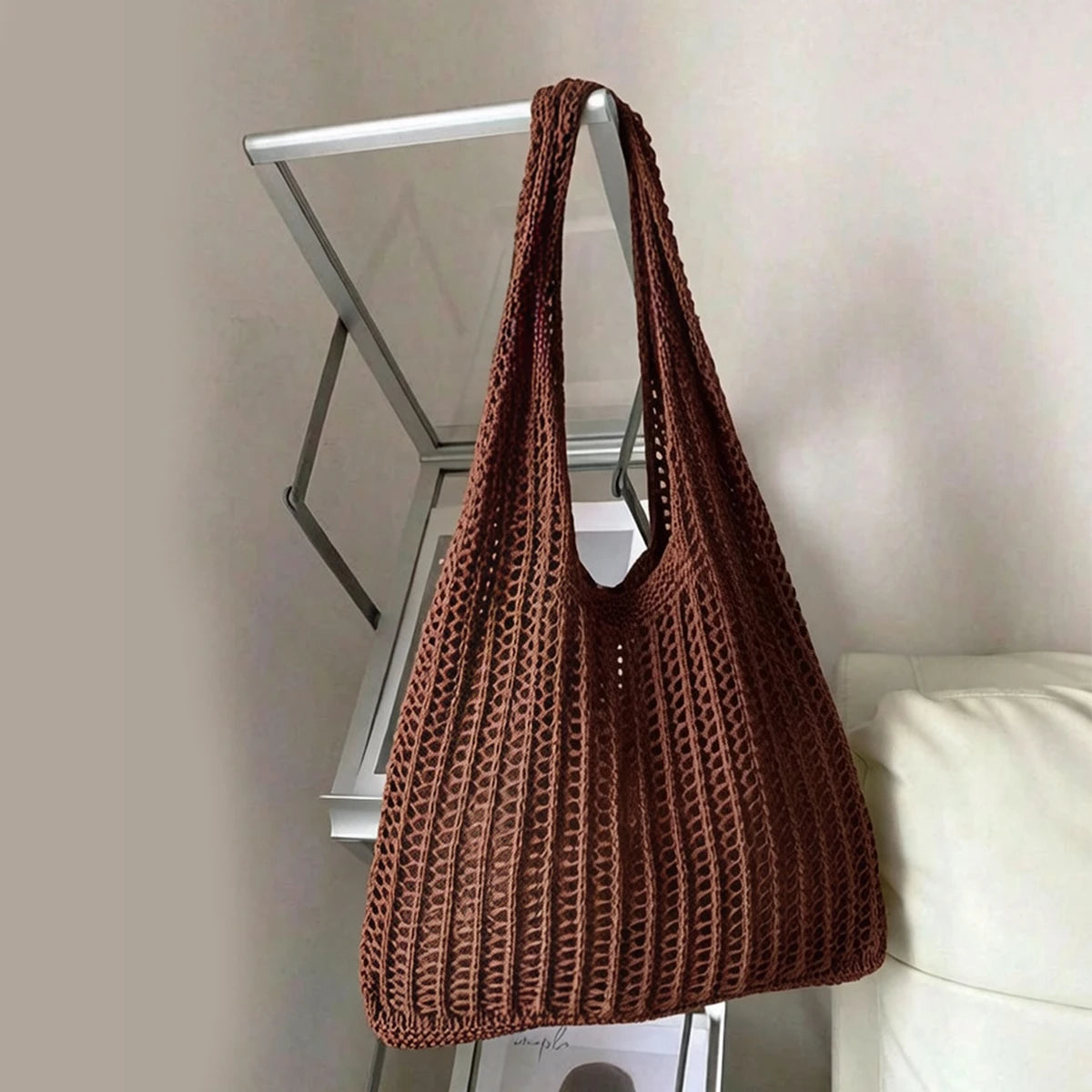 A brown knit shoulder bag hanging on a metal rack against a light wall.