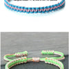 Handmade braided rope bracelet featuring pink and green threads, shown on a dark surface.
