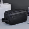A black leather toiletry bag with a zipper and strap is placed next to a white ceramic sink.