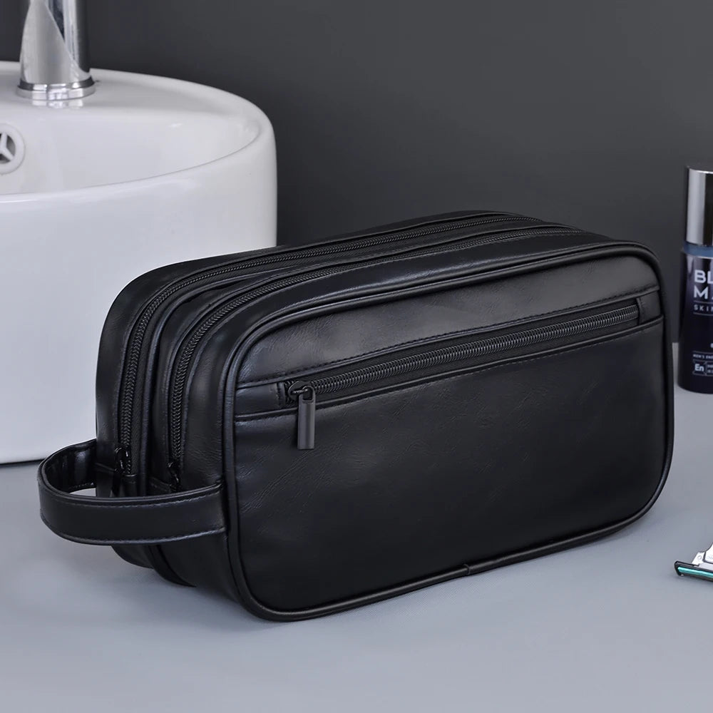 A black leather toiletry bag with a zipper and strap is placed next to a white ceramic sink.