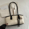 A beige leather tote bag with black handles and gold hardware resting on a white textured surface.