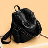 Sac à dos en cuir souple noir rivetée de luxe posé sur une surface en bois clair.