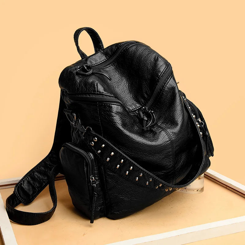 Sac à dos en cuir souple noir rivetée de luxe posé sur une surface en bois clair.