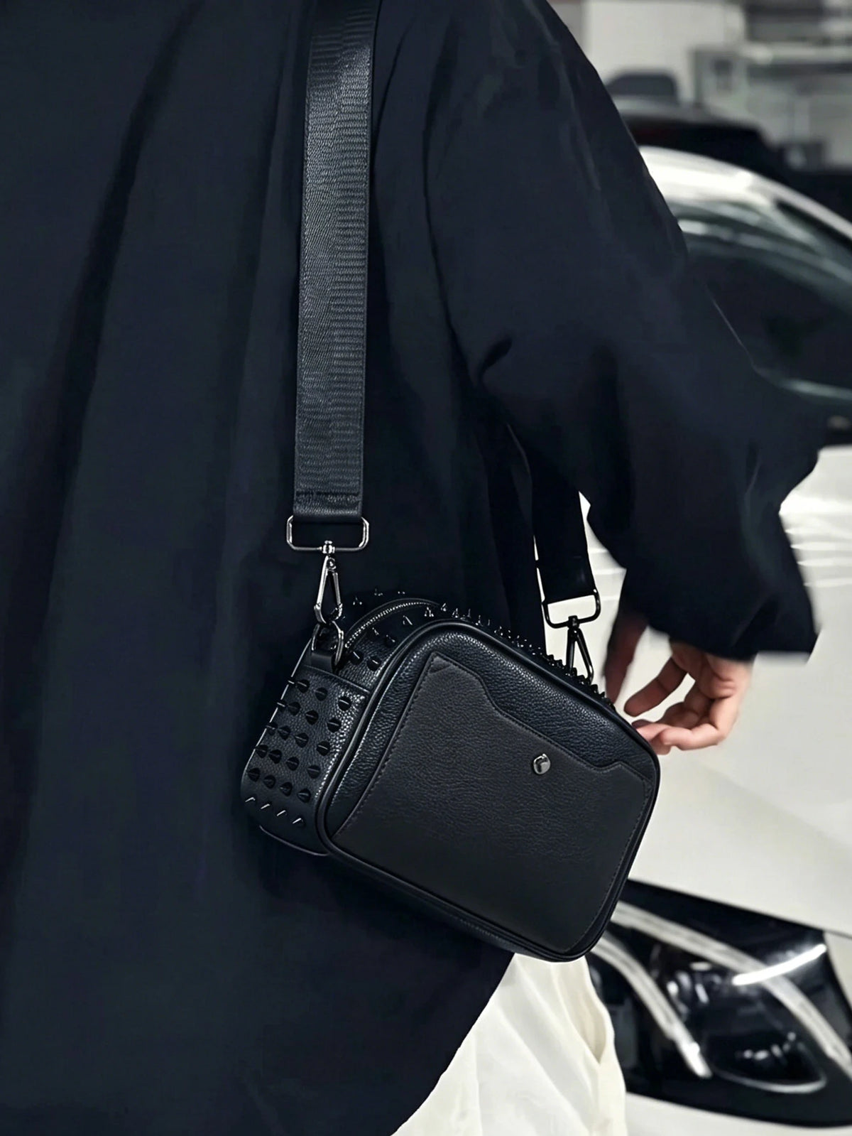 A black punk rivet studded crossbody sling bag worn by a person in a black coat.