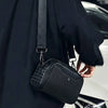 A black punk rivet studded crossbody sling bag worn by a person in a black coat.