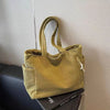 A mustard green corduroy shoulder bag with a zipper is displayed on a dark surface.