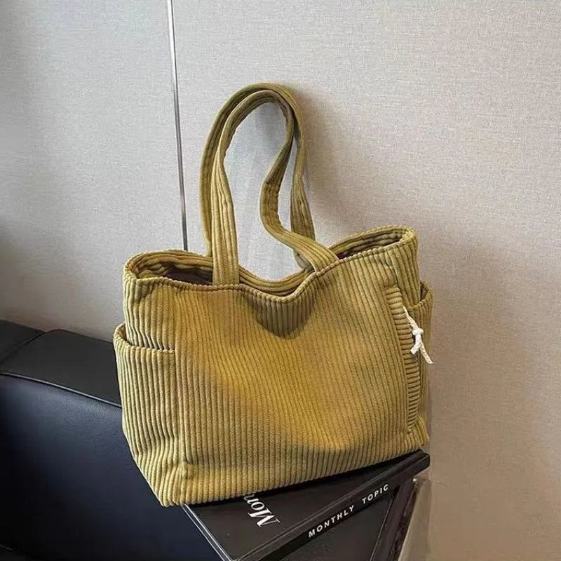 A mustard green corduroy shoulder bag with a zipper is displayed on a dark surface.