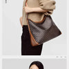 A woman is holding a brown leather geometric embroidery hobo shoulder bag against a light beige sweater and black pants.