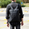 A person wearing a black denim jacket and dark pants is shown from the back carrying a black full-grain leather backpack.