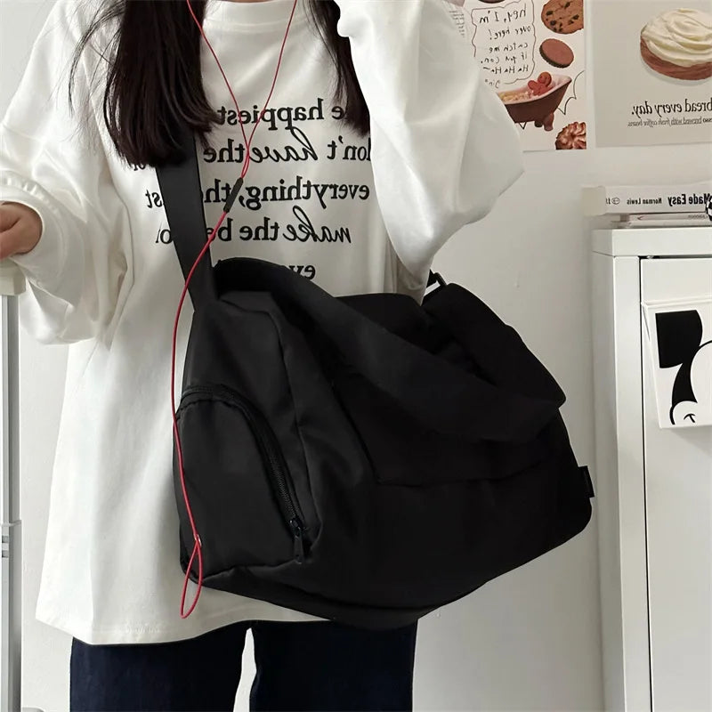A black canvas crossbody travel tote bag is shown hanging on a white shirt in a bright indoor setting.